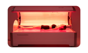 Woman lying in a red light therapy bed for photobiomodulation treatment.