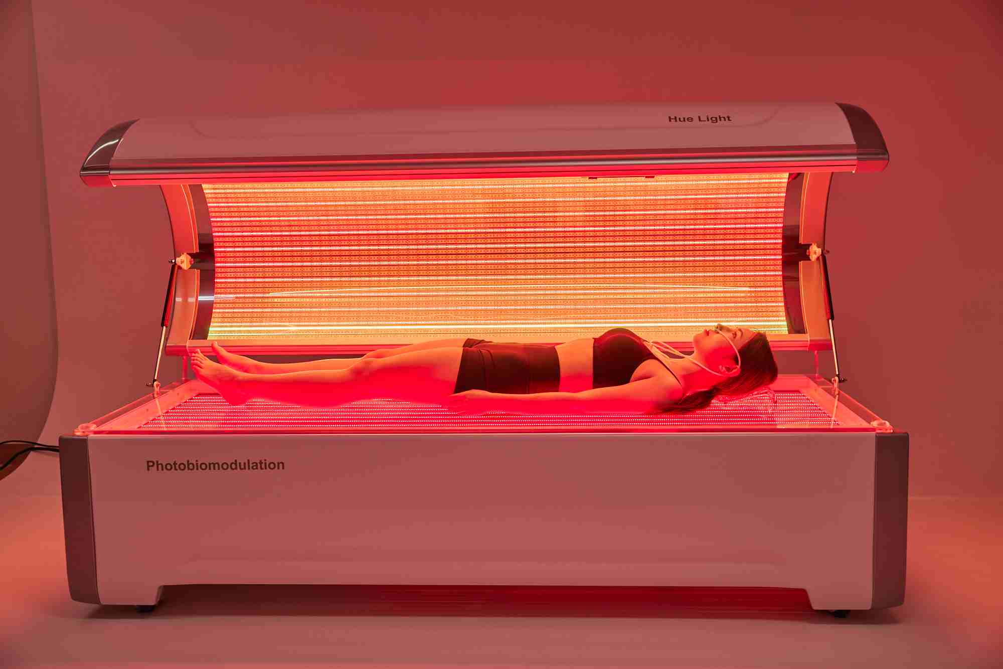 Woman lying in a red light therapy bed for photobiomodulation treatment